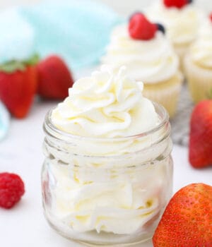 A small glass jar filled with beautifully piped frosting. The jar is surrounded by berries