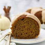 A slice of moist pumpkin cake with a glaze, and two gold forks hanging off the white plate