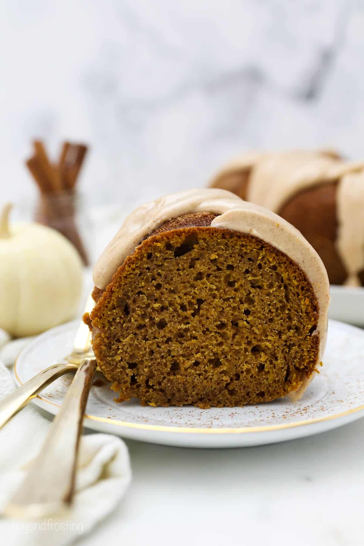A slice of moist pumpkin cake with a glaze, and two gold forks hanging off the white plate