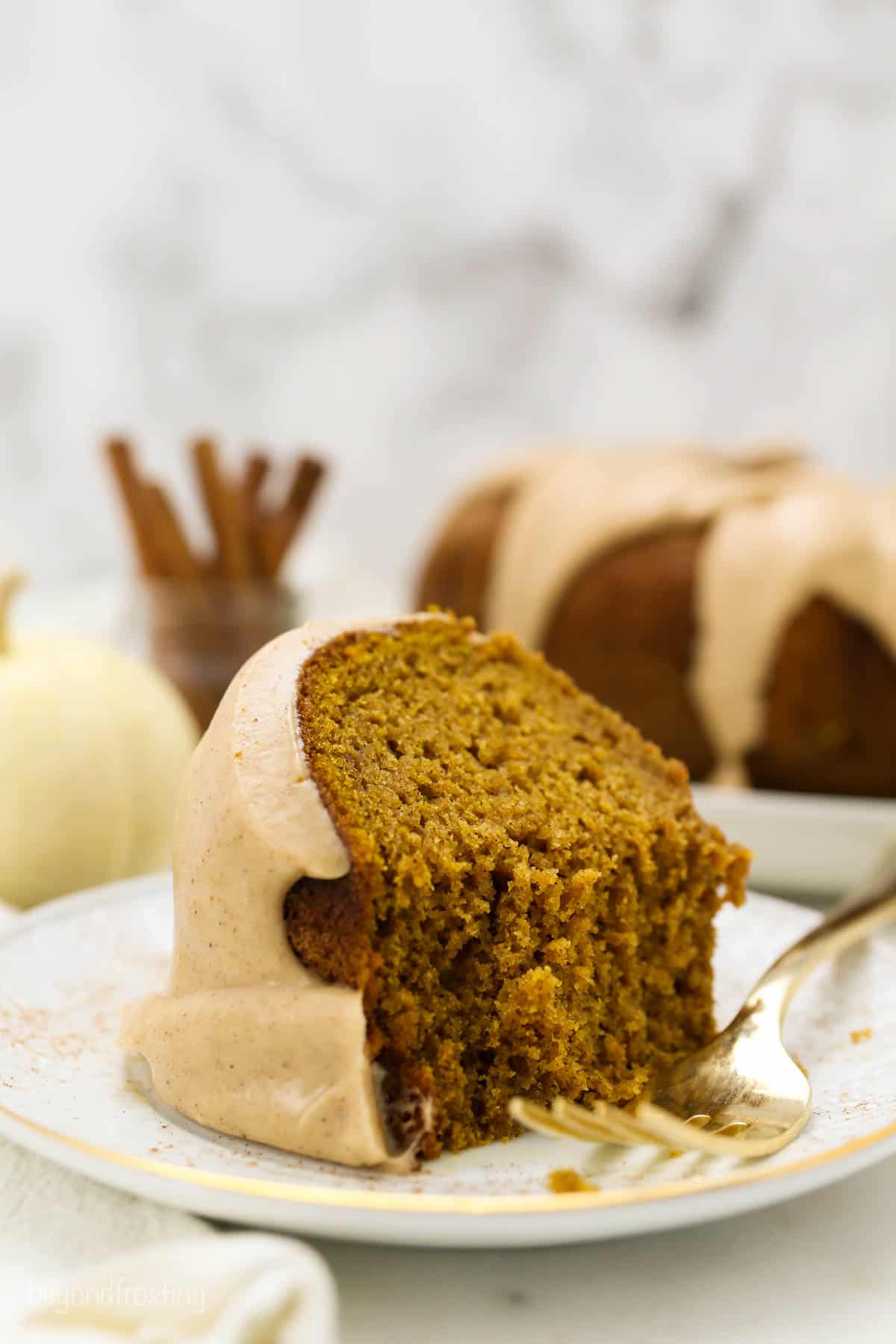 A slice of pumpkin cake on a white gold rimmed plate with a few bites taken our of it and a gold fork resting on the plate