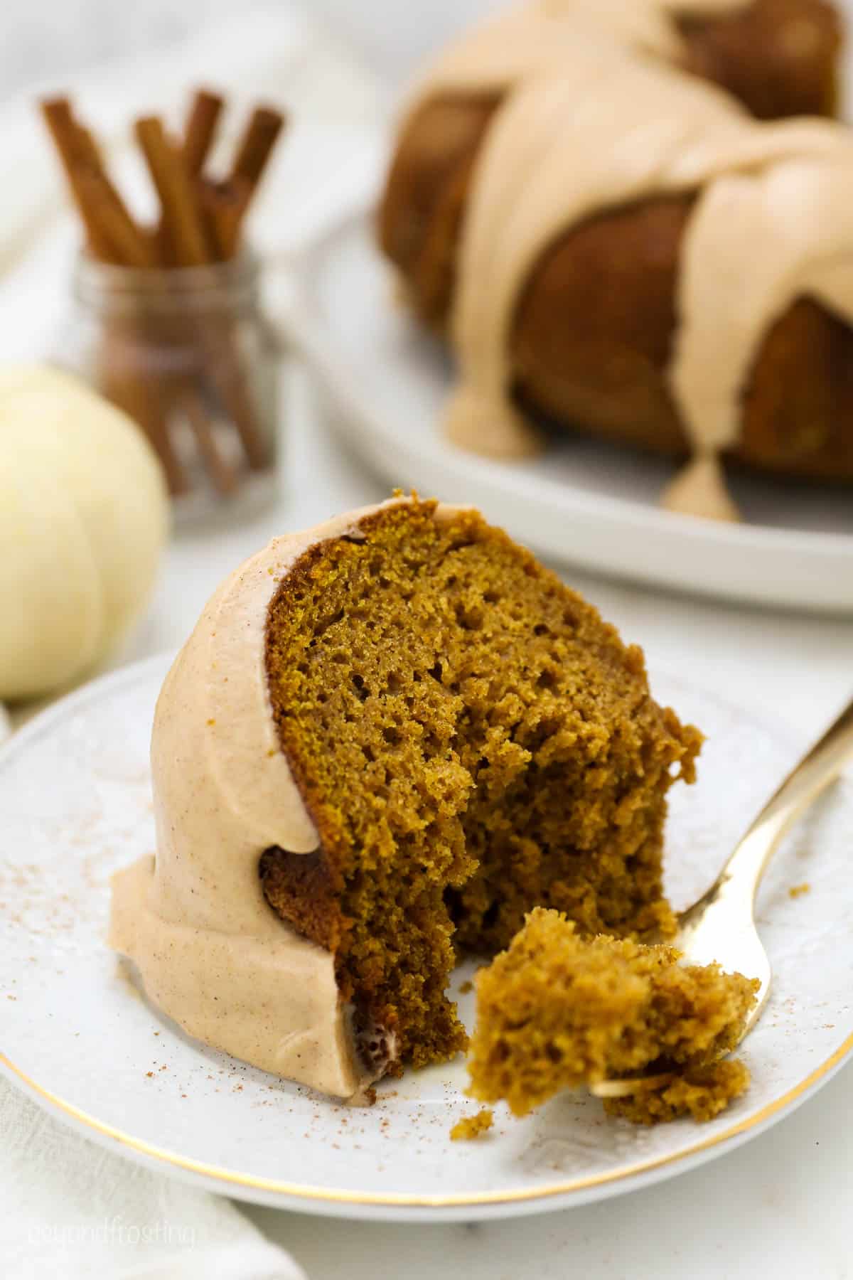 A slice of pumpkin cake on a white gold rimmed plate with a few bites taken our of it
