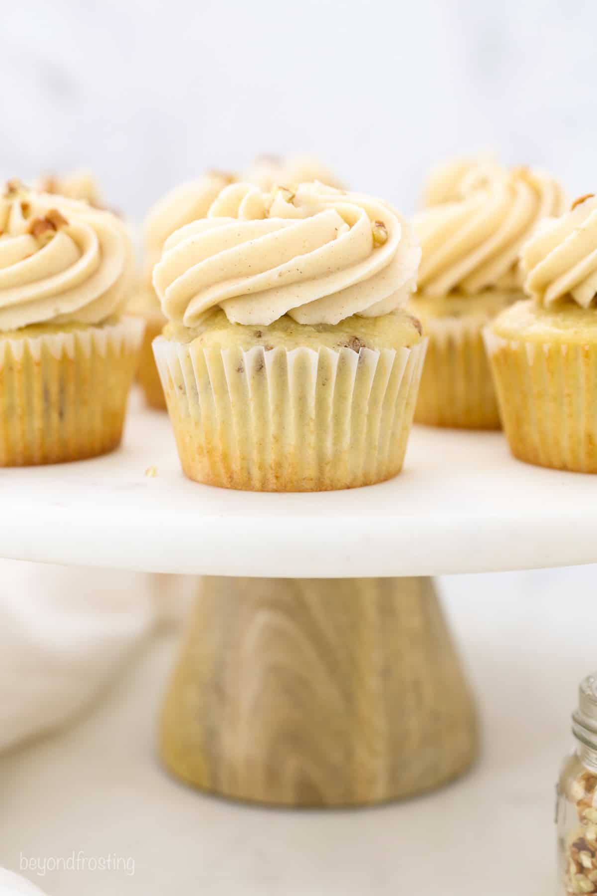 These homemade pecan cupcakes are filled with buttermilk, brown sugar, and buttery toasted pecans, finished with sweet maple buttercream. Frosted pecan cupcakes on a cake stand.