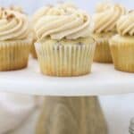 A marble cake stand with a wooden base is topped with pecan cupcakes