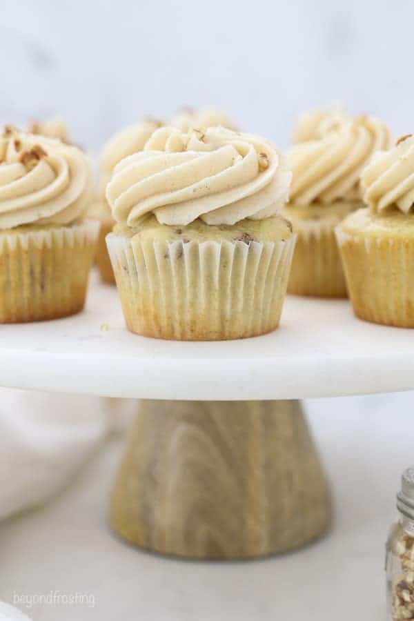 A marble cake stand with a wooden base is topped with pecan cupcakes