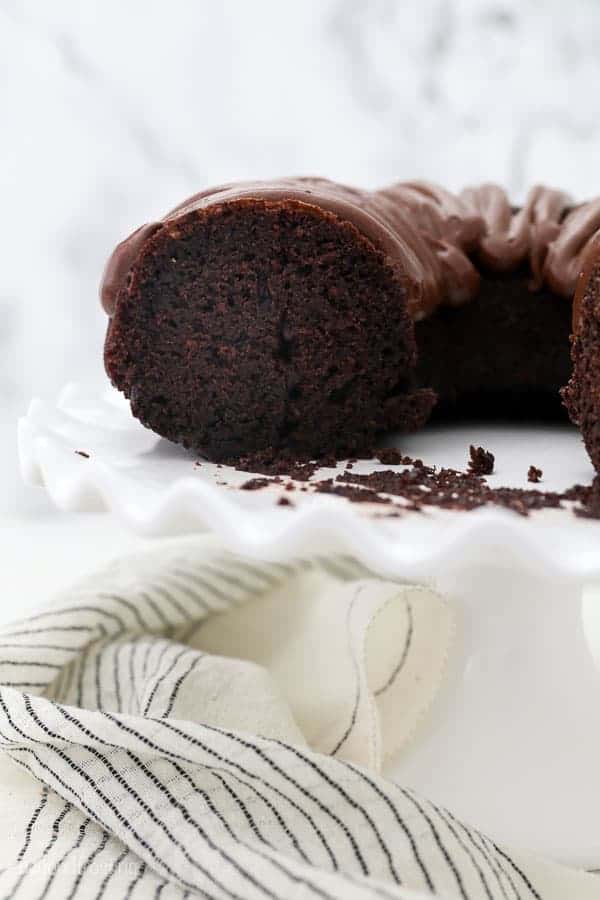 A white ruffled cake stand with a chocolate bundt cake with slices missing to show the inside of the cake