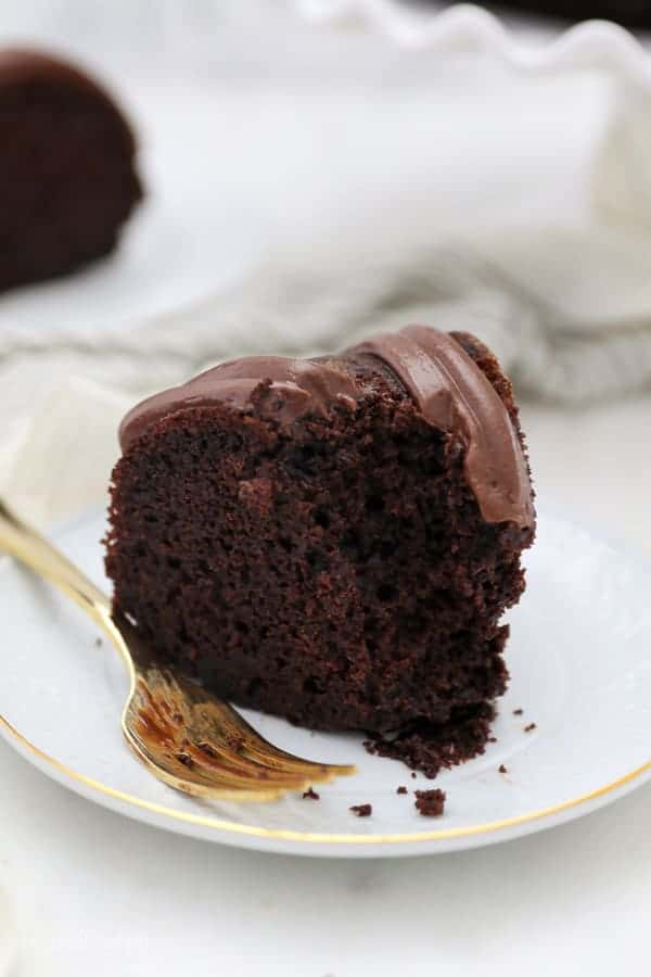 A slice of chocolate cake with bites missing with a gold fork resting on a white plate