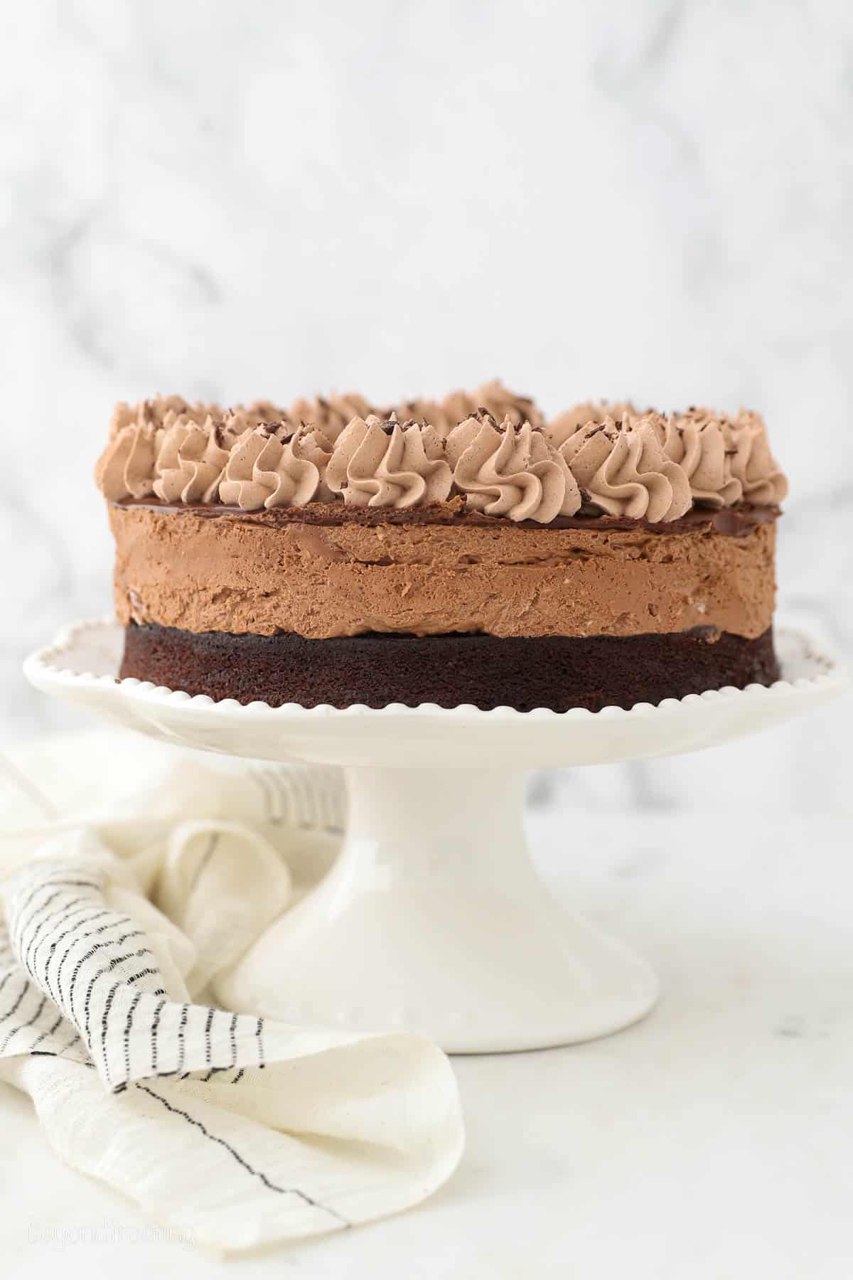 A whole chocolate mousse cake on a white ruffled cake stand.