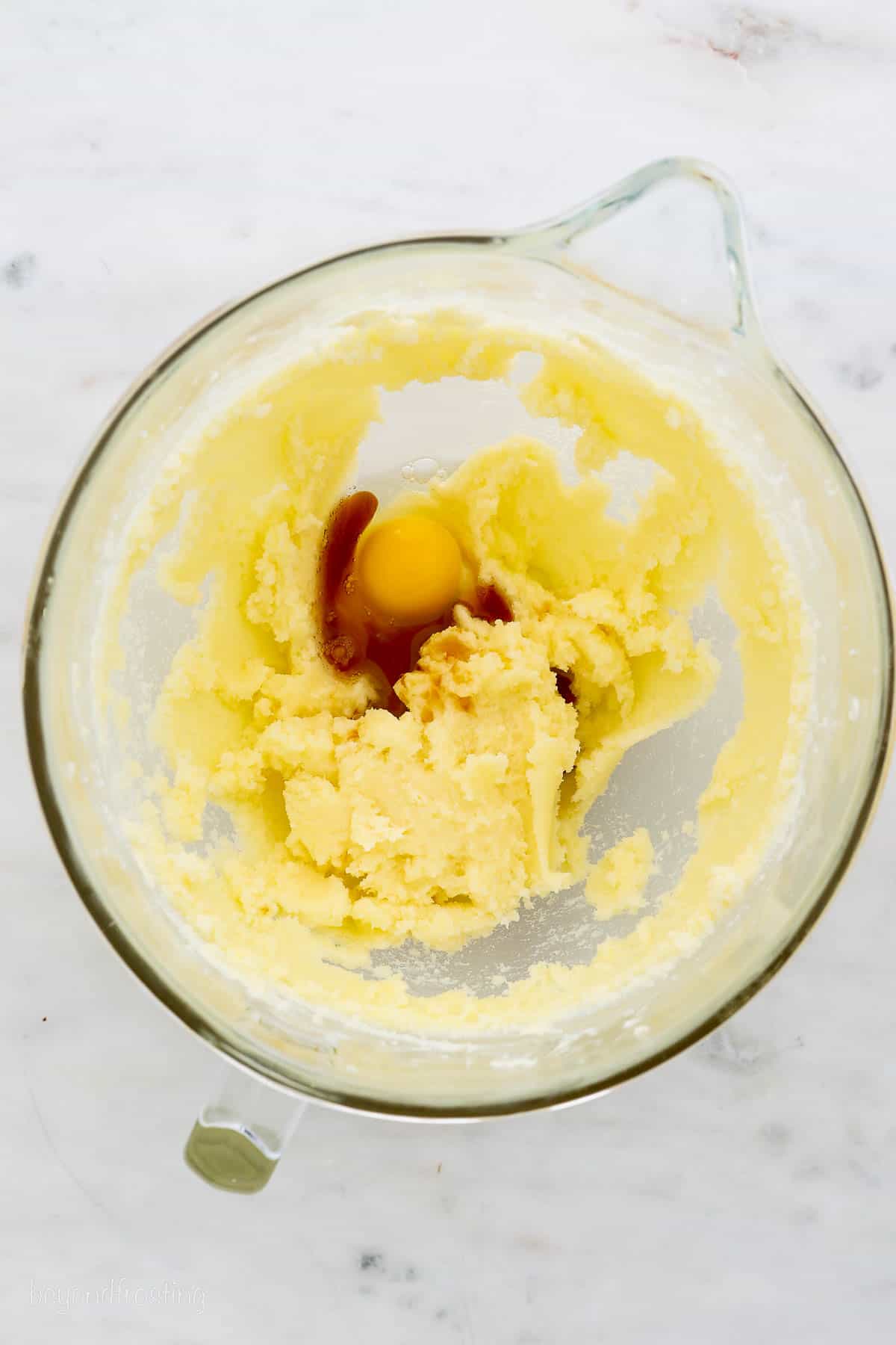 Eggs and vanilla added to creamed butter and sugar in a glass mixing bowl.