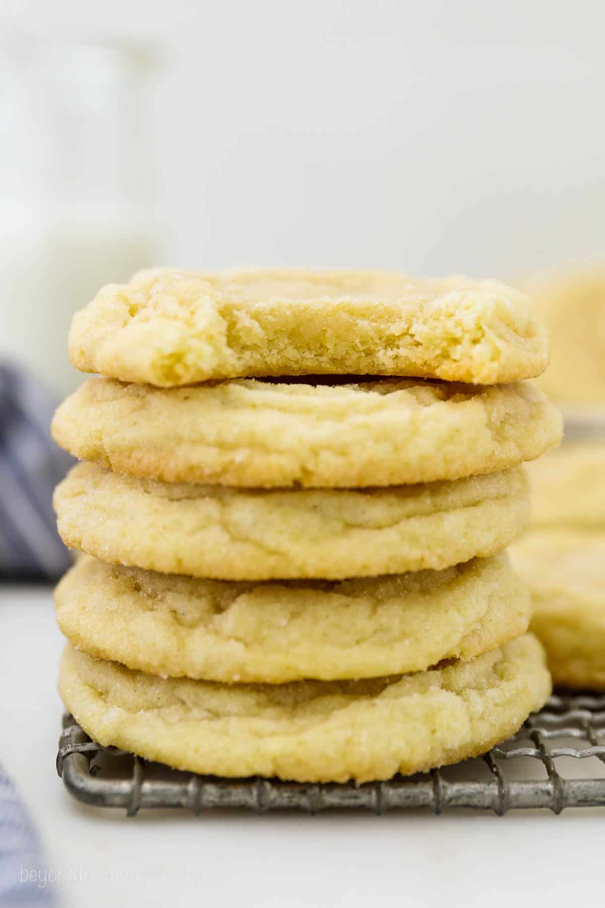 A stack of five soft sugar cookies with a bite missing from the top cookie.