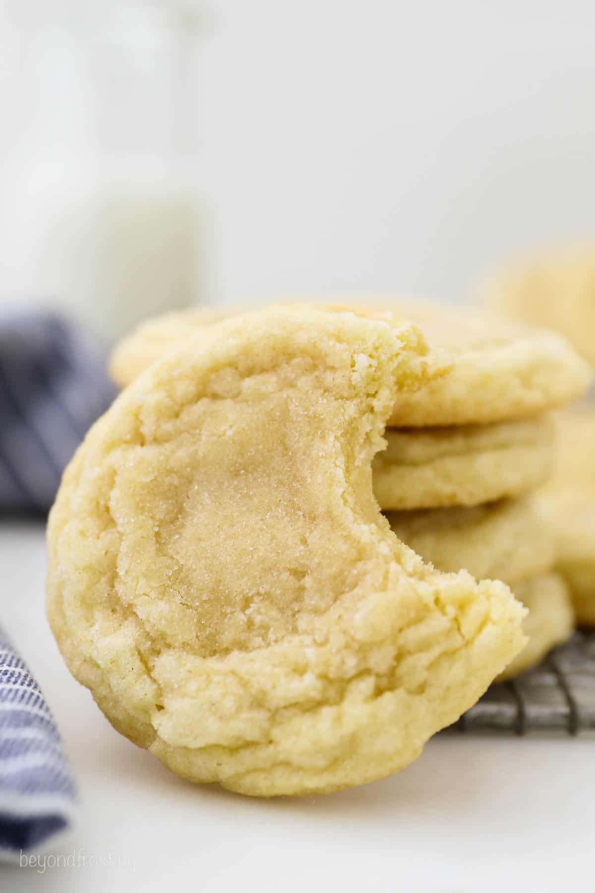 A soft sugar cookie with a bite missing, leaning against a stack of sugar cookies.