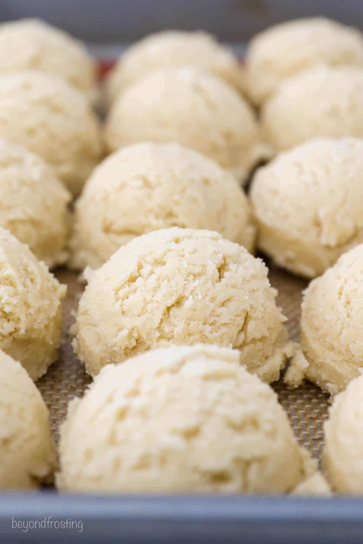 Scoops of drop sugar cookie dough lined up in rows on a metal baking sheet.