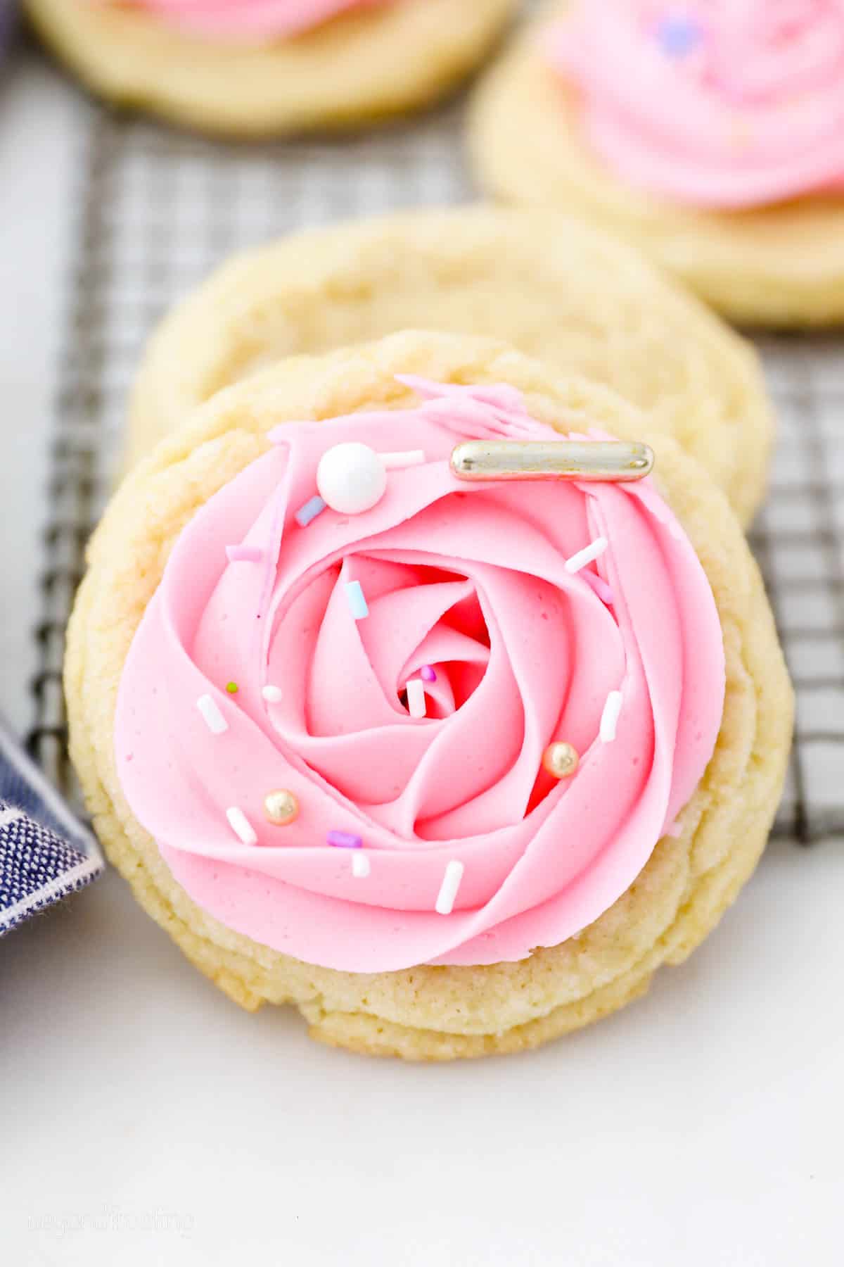 Close up of a soft sugar cookie decorated with a pink frosting swirl and sprinkles.