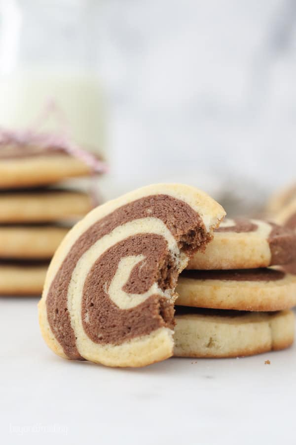 A pinwheel cookie with a bite taken out of it leaning against another stack of cookies