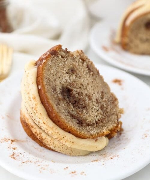 A slice of a bundt cake laying on a white plate that has been dusted with cinnamon