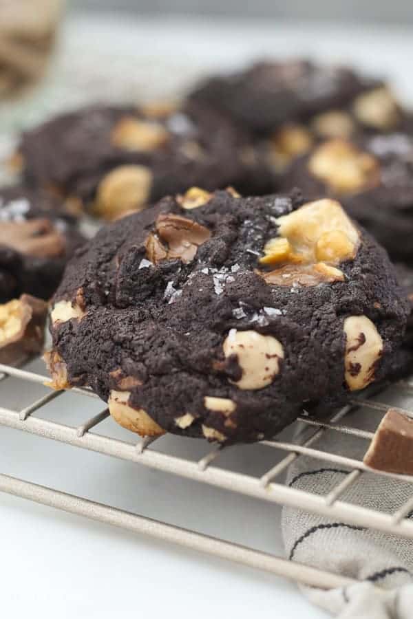 A chocolate cookie sitting on a wire rack with a melted snickers in the middle