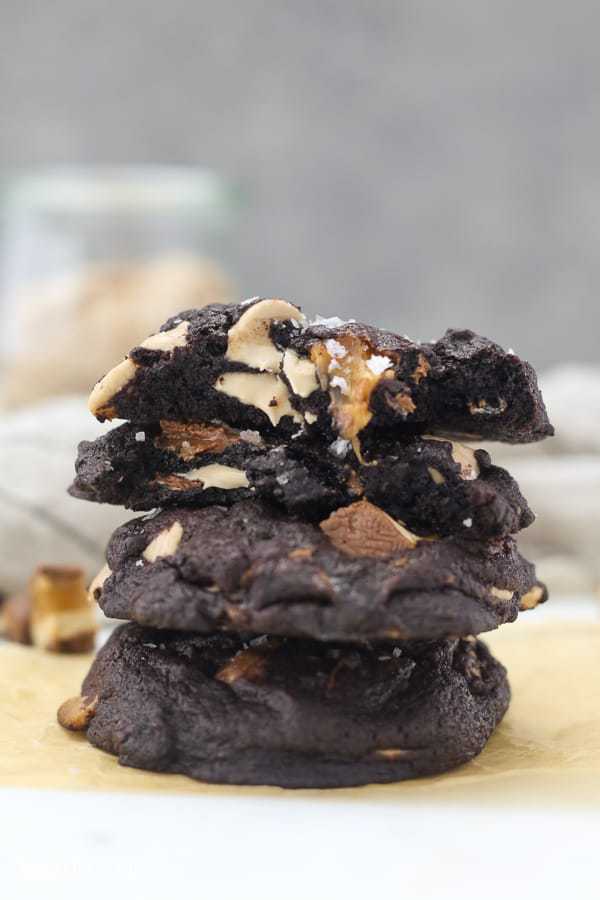A stack of 4 chocolate cookies with the top 2 broken in half showing the gooey caramel center
