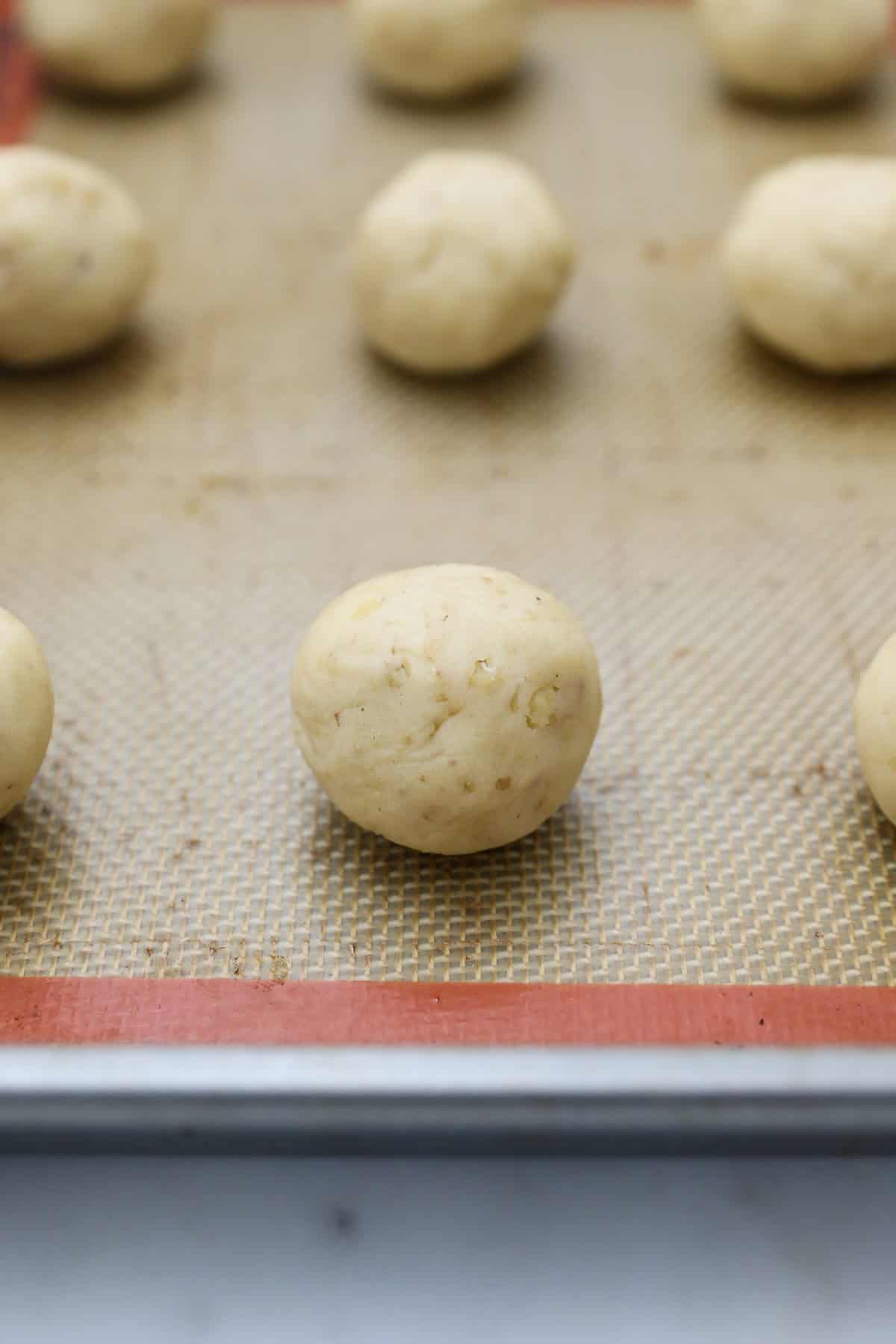 Snowball cookies are easy Christmas cookies made with buttery shortbread and chopped nuts, rolled in powdered sugar to look like snowballs! Close up of unbaked snowball cookies on a baking sheet.