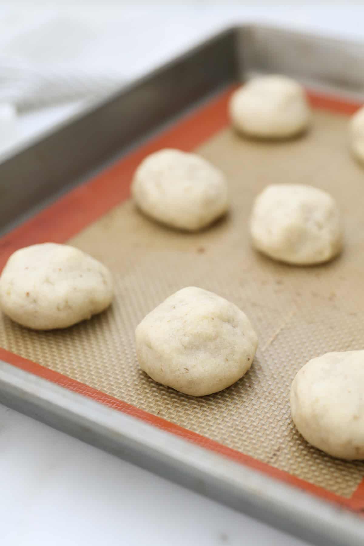 Snowball cookies are easy Christmas cookies made with buttery shortbread and chopped nuts, rolled in powdered sugar to look like snowballs! Close up of baked snowball cookies on a baking sheet before being rolled in powdered sugar.