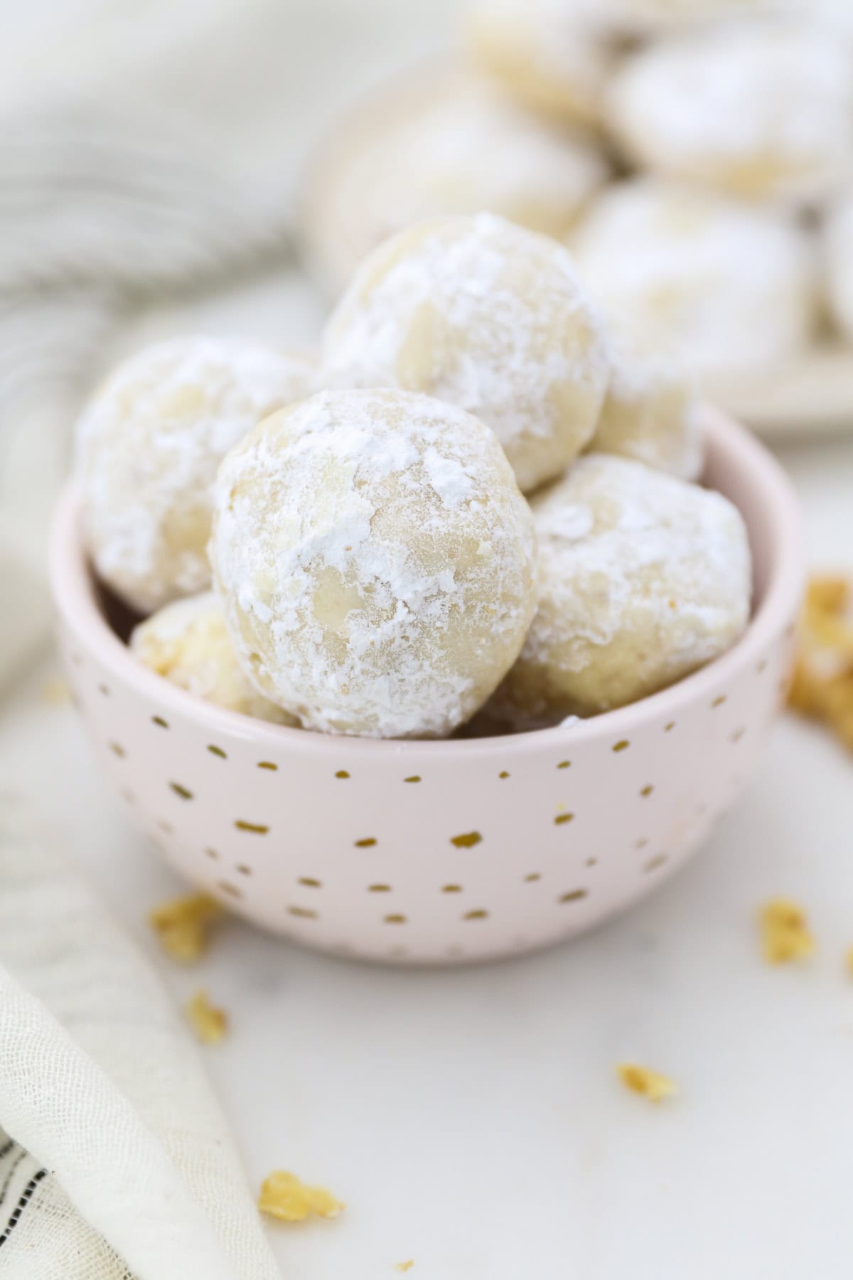 Snowball cookies are easy Christmas cookies made with buttery shortbread and chopped nuts, rolled in powdered sugar to look like snowballs! Snowball cookies piled in a small pink dish with gold polka dots.