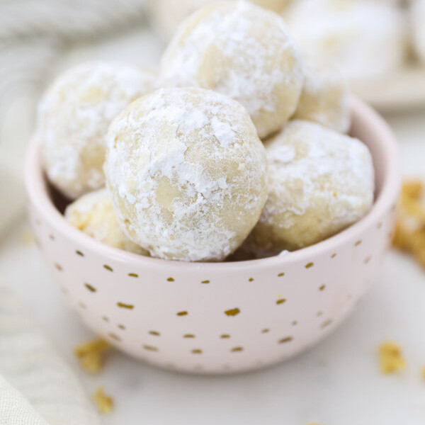 A small pink dish with gold polka dots is filled with Mexican Wedding Cookies