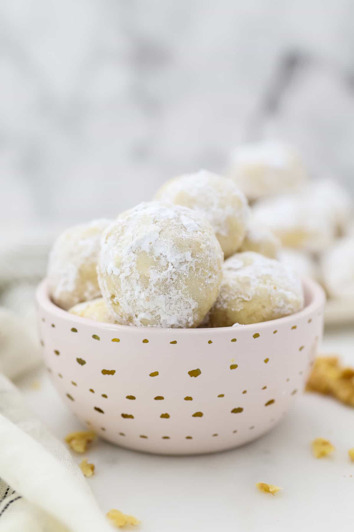 Snowball cookies are easy Christmas cookies made with buttery shortbread and chopped nuts, rolled in powdered sugar to look like snowballs! A small pink dish with gold polka dots filled with snowball cookies.