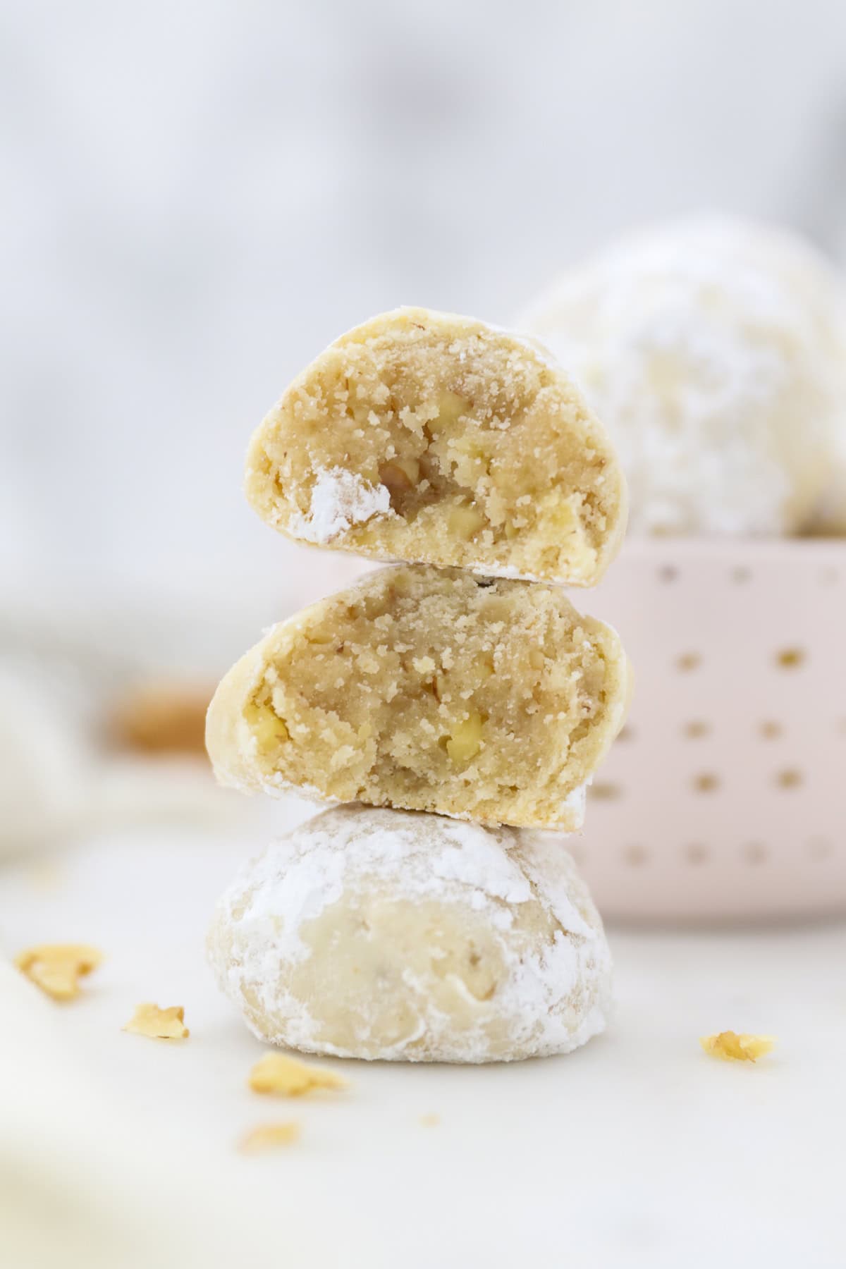 Snowball cookies are easy Christmas cookies made with buttery shortbread and chopped nuts, rolled in powdered sugar to look like snowballs! A snowball cookie broken in half showing the buttery interior, stacked on top of another cookie.