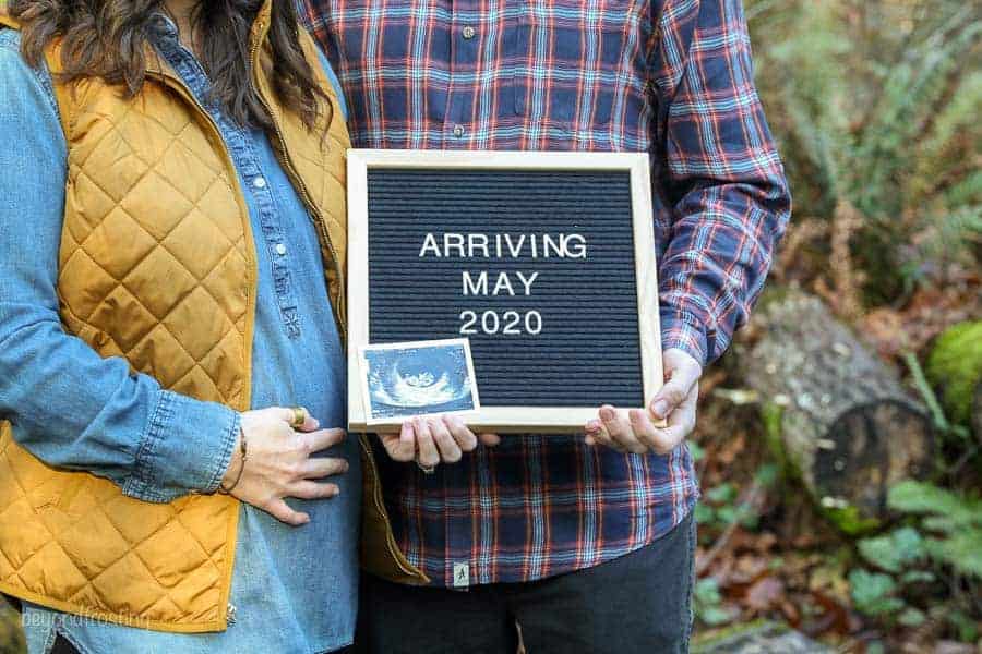 A baby announcement with the husband and wife holding a letter board that say Arriving May 2020