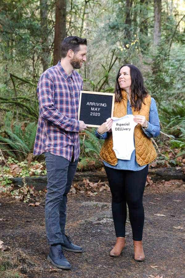 A baby announcement with the husband and wife holding a letterboard and a onesie