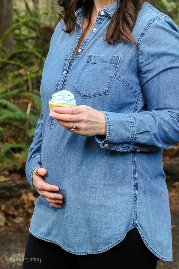 A pregnant women holding her stomach and a blue cupcake