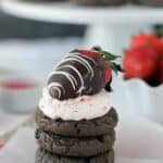 A stack of chocolate cookies and the cookie on top has strawberry frosting and a chocolate covered strawberry on top