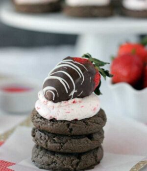 A stack of chocolate cookies and the cookie on top has strawberry frosting and a chocolate covered strawberry on top