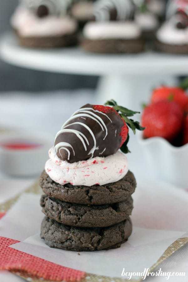 A stack of chocolate cookies and the cookie on top has strawberry frosting and a chocolate covered strawberry on top