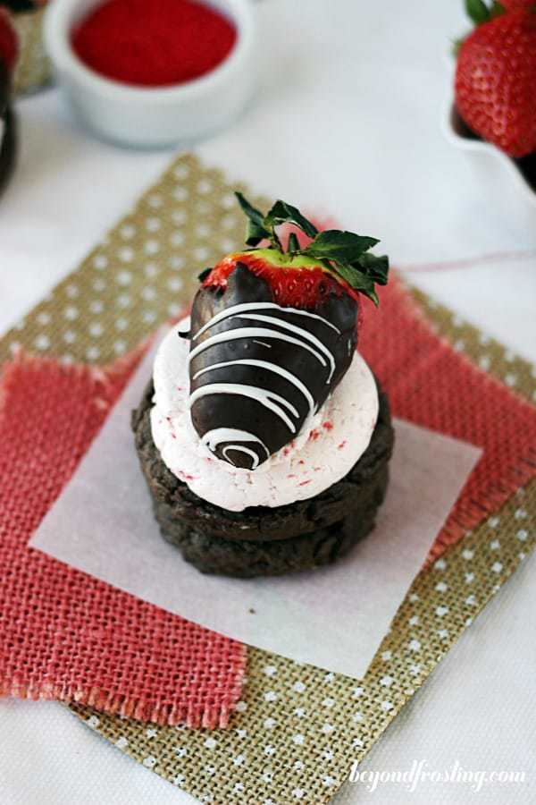 An overhead shot of a chocolate covered strawberry on top of a chocolate cookie that sitting on some polka dot burlap