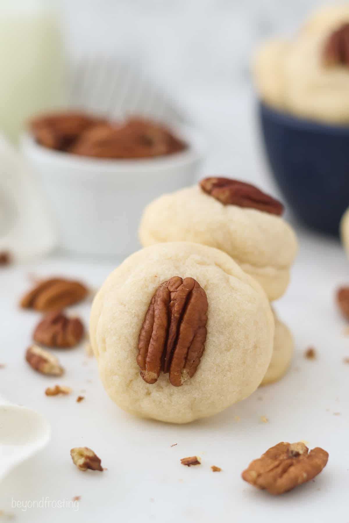 A cream cheese cookie garnished with a pecan propped up against two cookies stacked on top of one another.