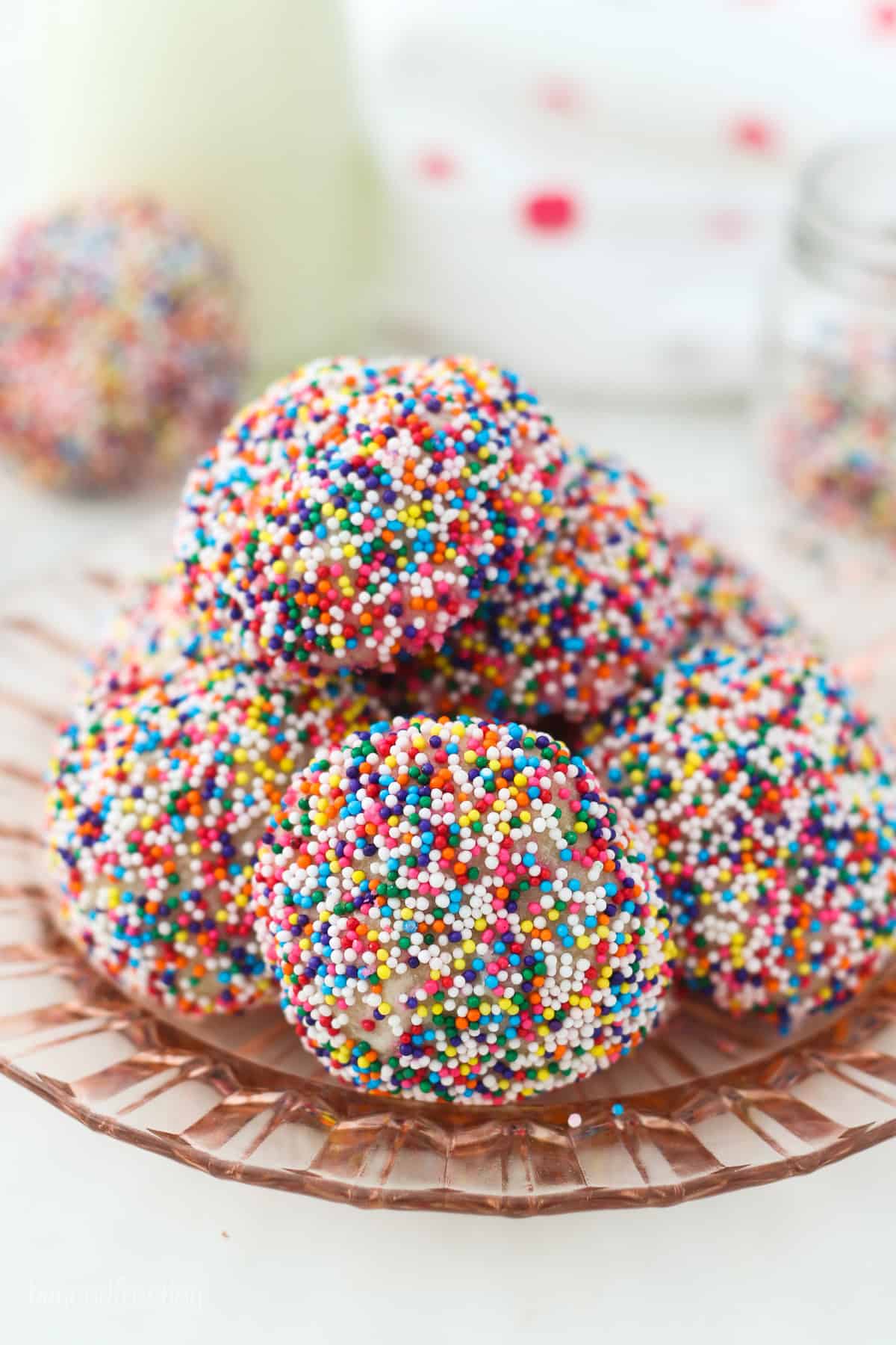 Sprinkle-covered cream cheese cookies piled onto a glass plate.
