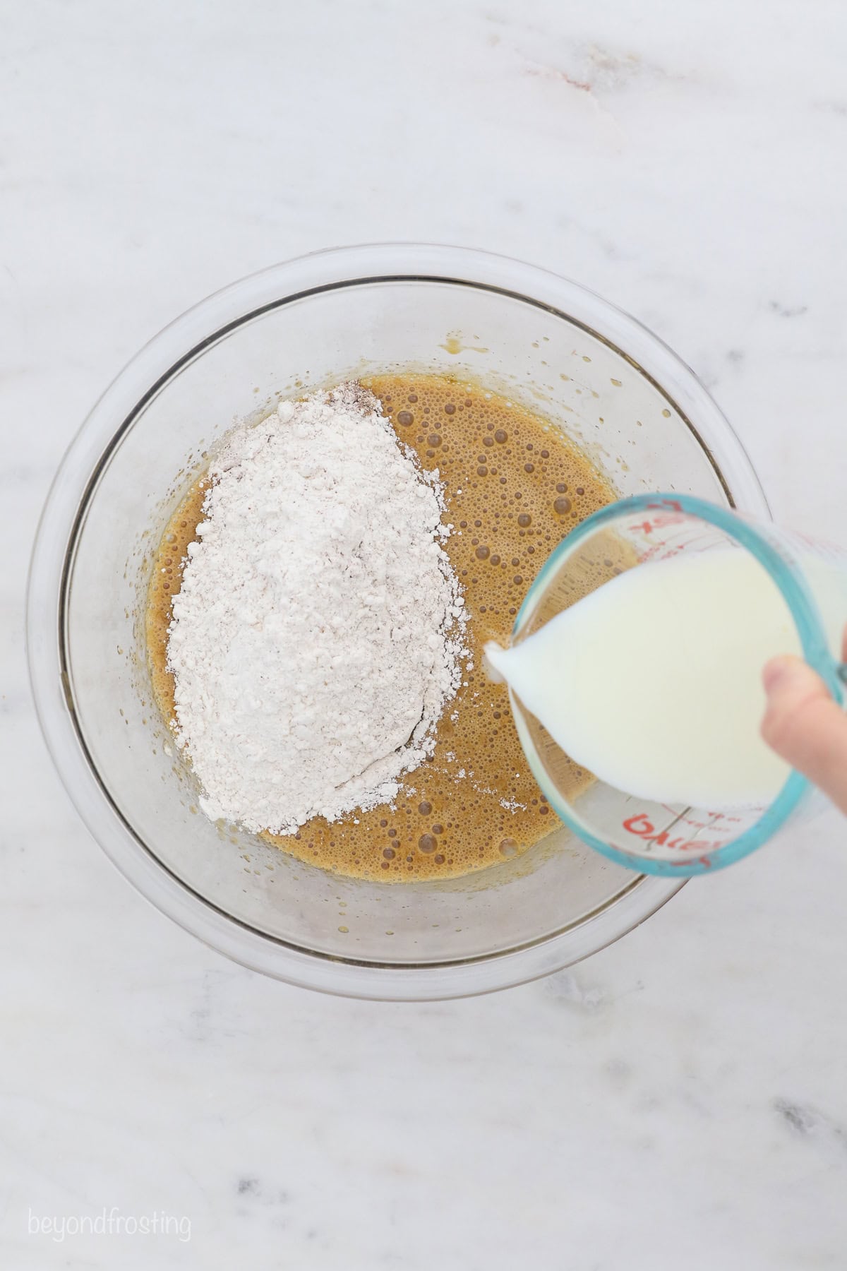 Buttermilk and flour added to cake batter in a glass bowl.