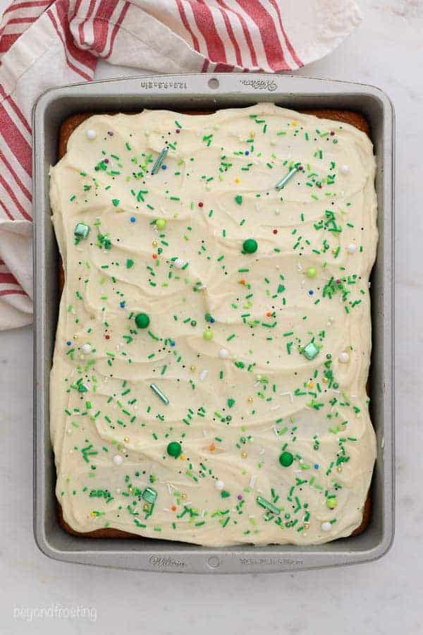 Swirled frosting covered with Christmas sprinkles on cake in a pan.