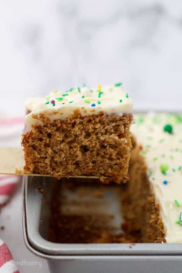 A cake server is holding a slice of gingerbread cake over top of the pan