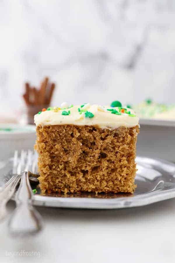 A tall slice of gingerbread cake with two silver forks sitting on a vintage silver plate