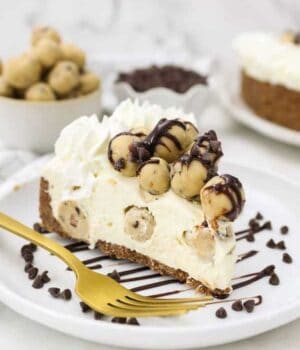 A gorgeous slice of cheesecake on a white plate loaded with cookie dough on top