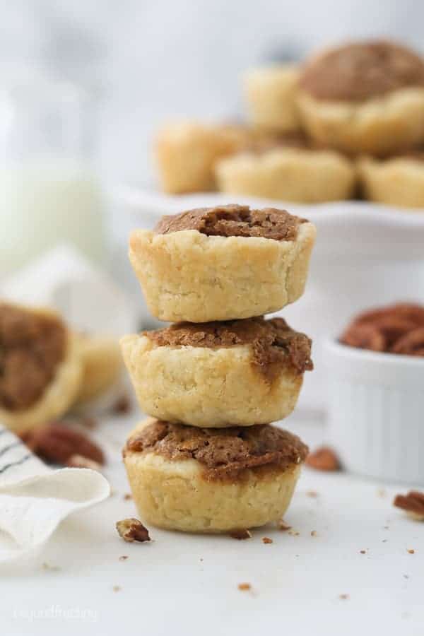 A stack of 3 mini pecan tarts with a small white cake stand blurred out in the background