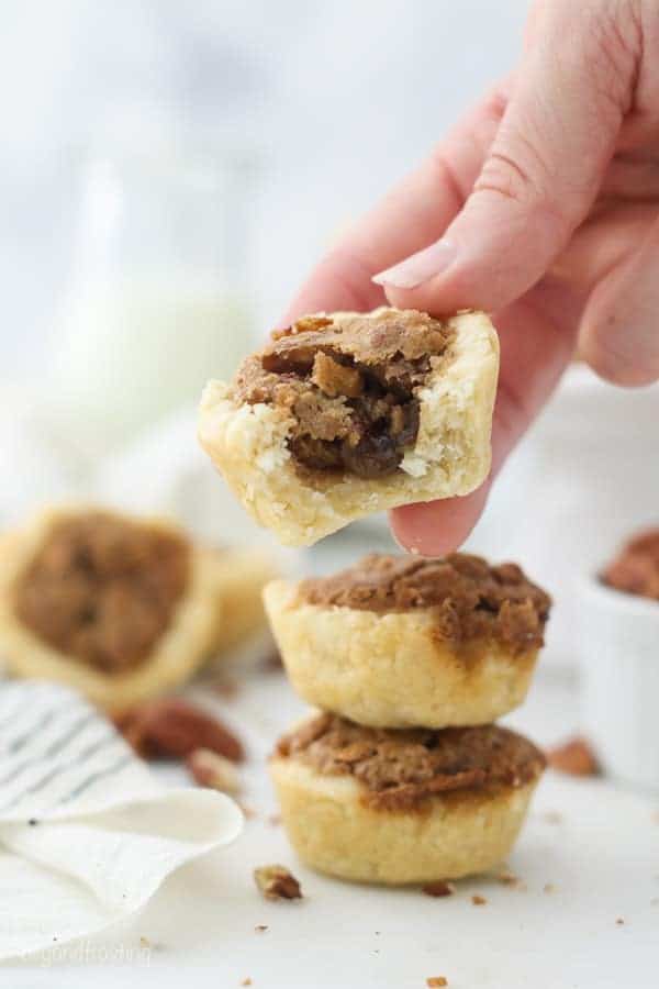 A hand holding a pecan tart with a bite taken out of it