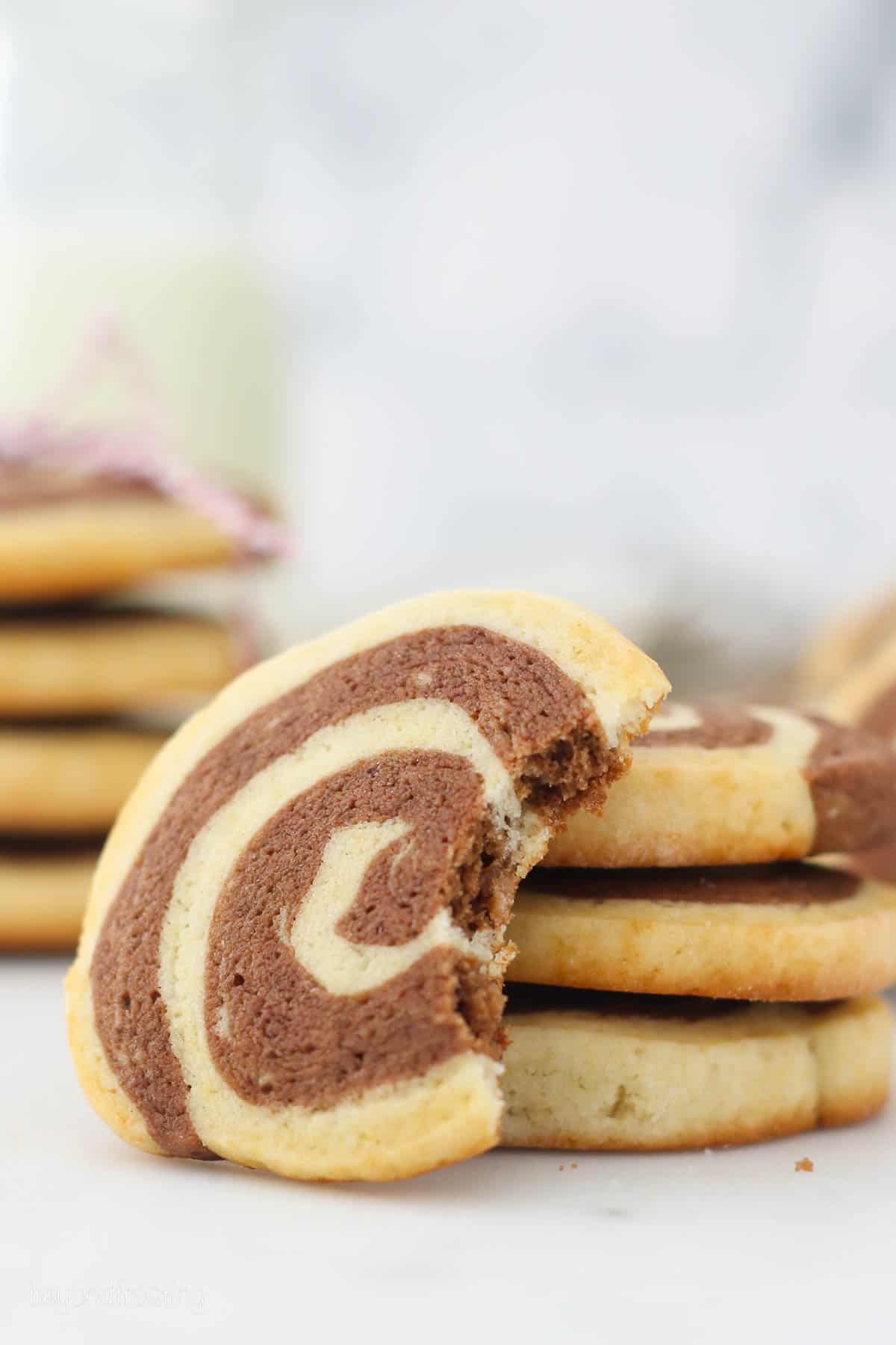 A pinwheel cookie with a bite missing propped up against a small stack of cookies.