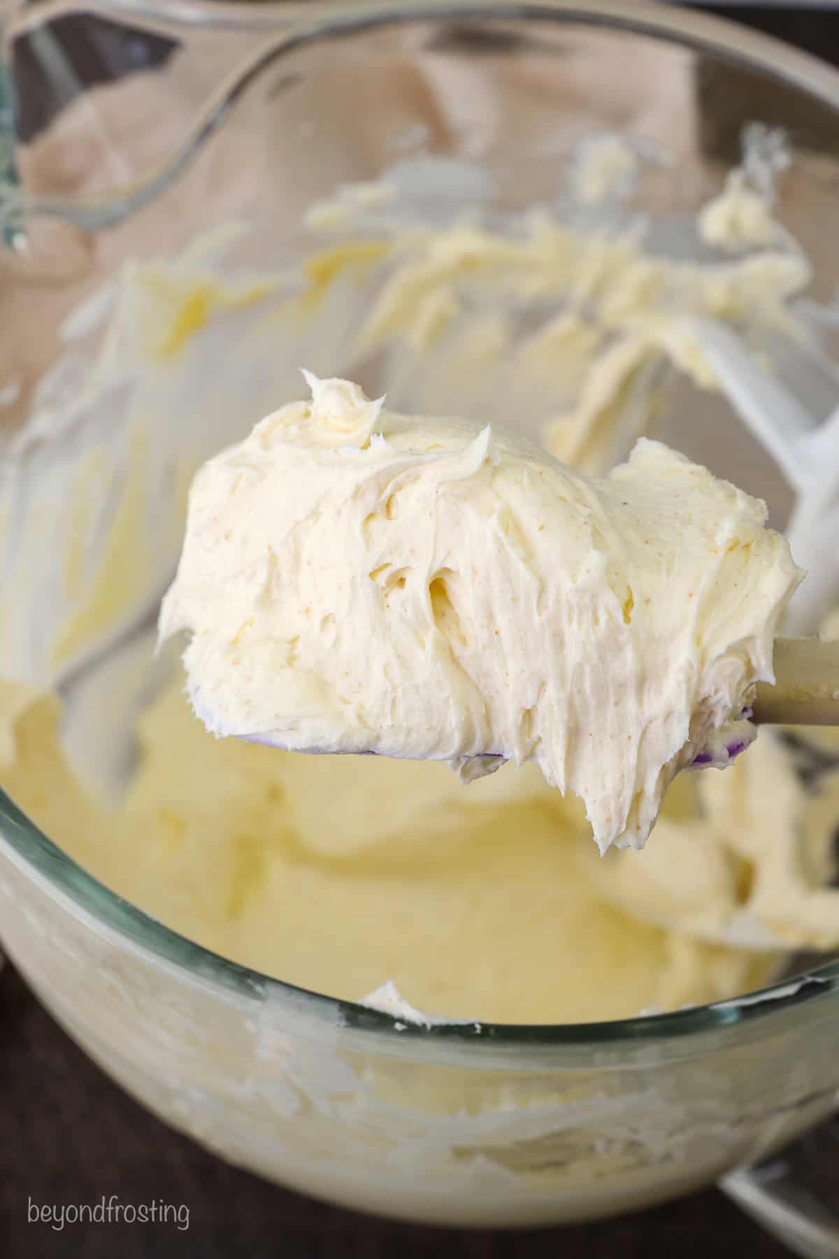 Close up of a spatula with frosting held over a mixing bowl.