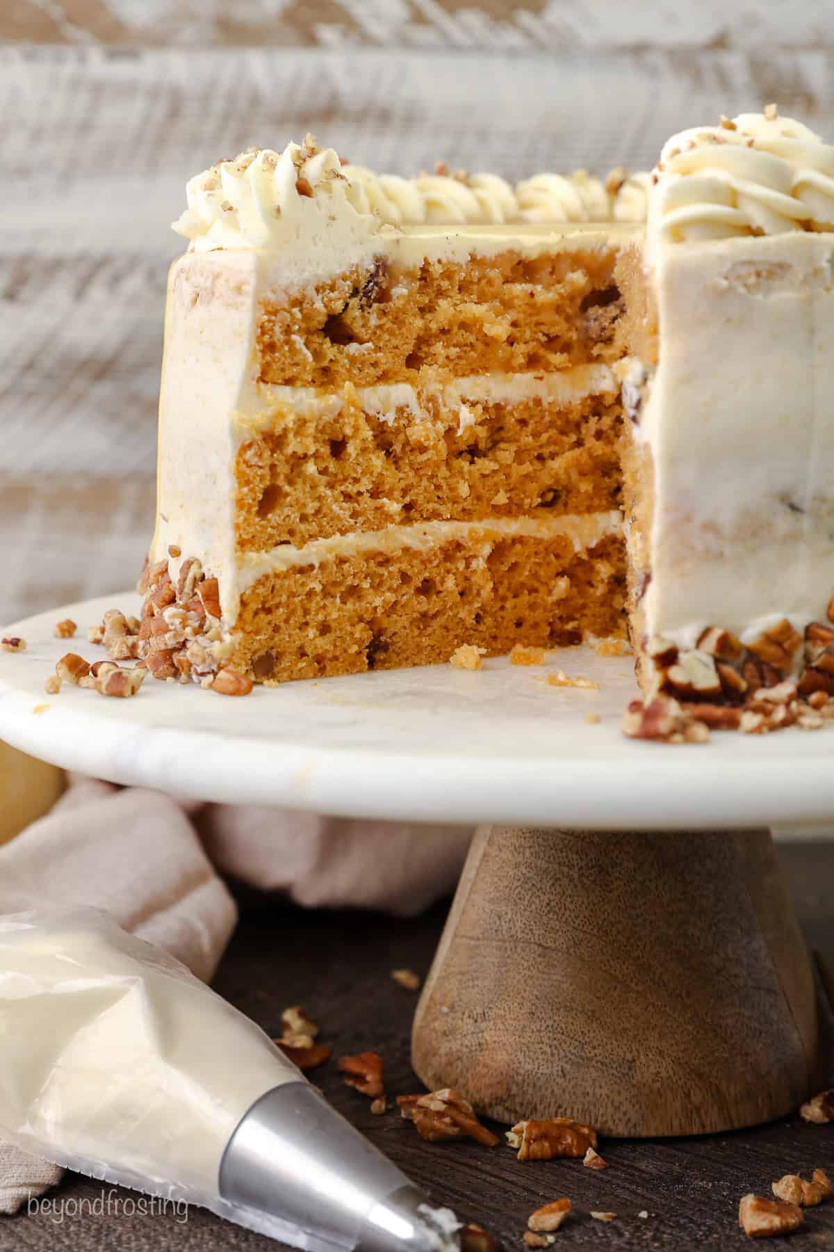 A frosted butterscotch cake with a large slice missing on a cake stand.