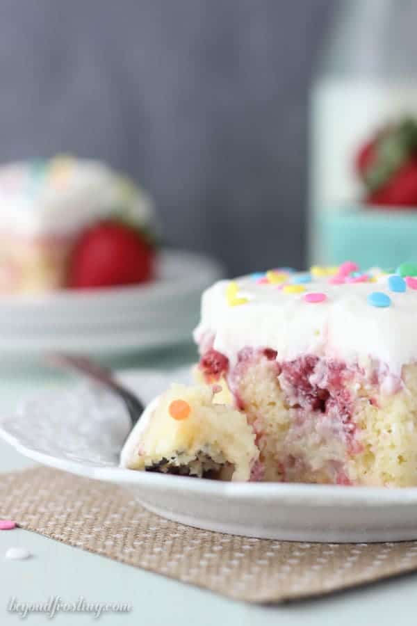 A pretty slice of strawberry cake with a fork laying on the plate, the fork has a bite of cake on it