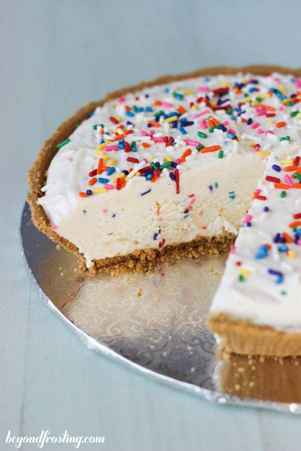 A whole ice cream pie with a slice missing sitting on a silver cake plate