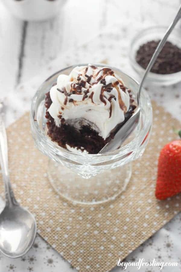 A small glass sundae cup with a cupcake and spoon in it, the cupcake has a bite taken out of it