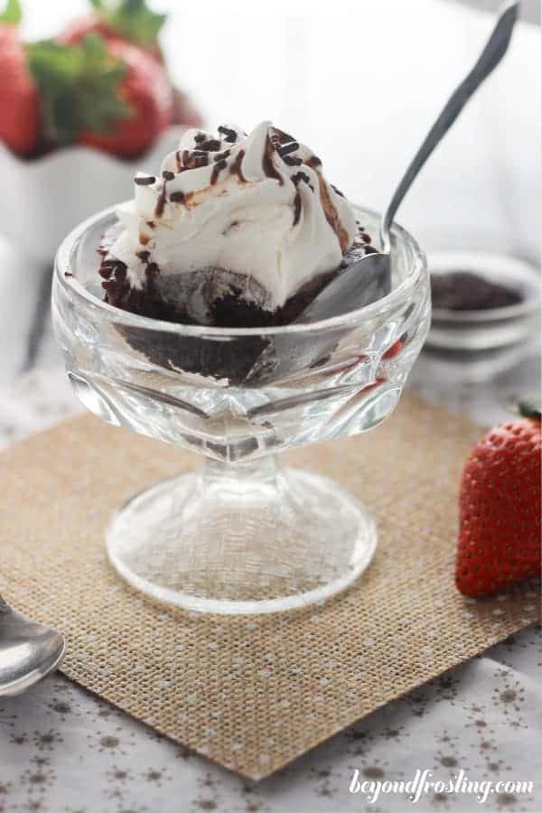 A small glass sundae cup with a cupcake and spoon in it, the cupcake has a bite taken out of it