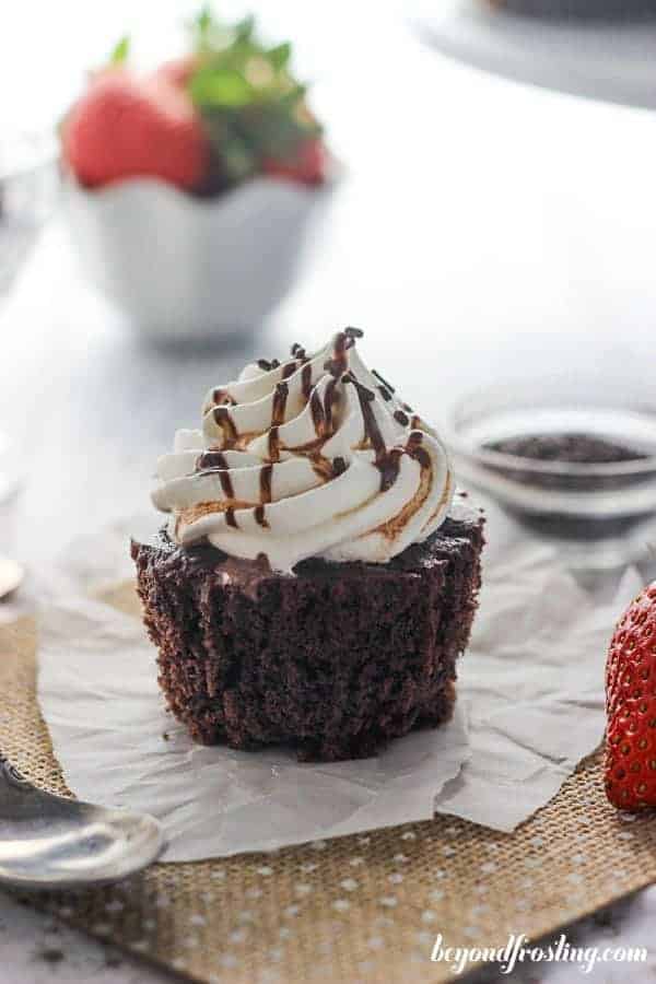 An unwrapped chocolate cupcake on a piece of burlap with a bowl of strawberries in the background
